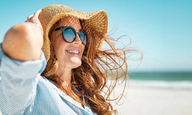 woman on a sunny beach wearing sunglasses and a sun hat