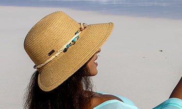 banner for organic sunscreen category featuring woman wearing hat on beach