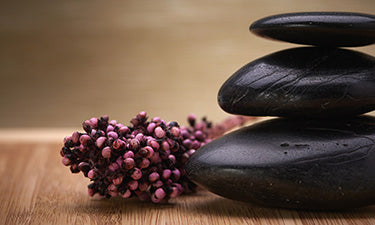 image for self care essentials category featuring smooth black pebbles and pink berries