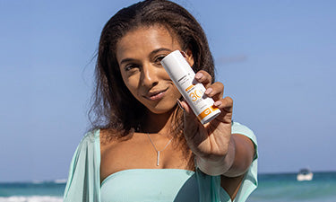 woman on beach holding travel-size sunscreen